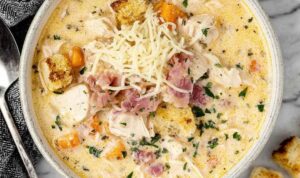 Bowl of creamy Chicken Cordon Bleu Soup topped with shredded Swiss cheese and fresh parsley