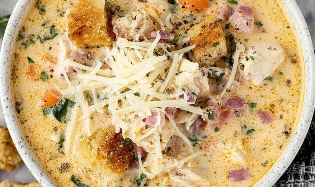 Bowl of creamy Chicken Cordon Bleu Soup topped with shredded Swiss cheese and fresh parsley