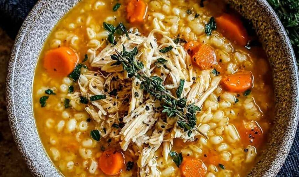 A bowl of chicken pastina soup with tiny pasta pearls, tender chicken pieces, and fresh parsley garnish