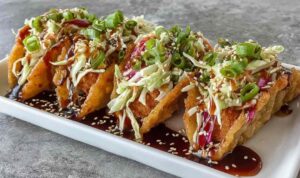 Crispy Chicken Wonton Tacos with Teriyaki Glaze Crispy chicken wonton tacos with teriyaki glaze topped with shredded cabbage, carrot matchsticks, and sesame seeds on a white plate