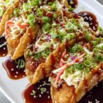 Crispy chicken wonton tacos with teriyaki glaze topped with shredded cabbage, carrot matchsticks, and sesame seeds on a white plate