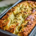 Sliced dill pickle bread loaf on a wooden cutting board with fresh dill and pickle chips