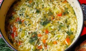 Bowl of easy orzo leek and dill soup garnished with fresh dill on a wooden table