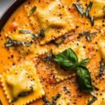 Easy Tuscan ravioli soup served in a white bowl topped with Parmesan cheese and fresh spinach