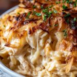 French Onion Chicken Orzo Casserole in a white baking dish with golden melted Gruyere cheese on top