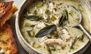 Bowl of garlic and sage chicken soup with shredded chicken, golden broth, and fresh sage leaves