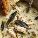 Bowl of garlic and sage chicken soup with shredded chicken, golden broth, and fresh sage leaves