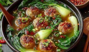 Ginger chicken meatball soup in a white bowl with baby bok choy and crispy wonton strips
