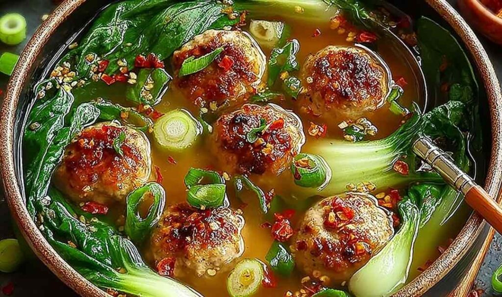 Ginger chicken meatball soup in a white bowl with baby bok choy and crispy wonton strips