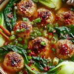 Ginger chicken meatball soup in a white bowl with baby bok choy and crispy wonton strips