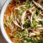 Bowl of ginger garlic chicken noodle soup topped with green onions and fresh cilantro