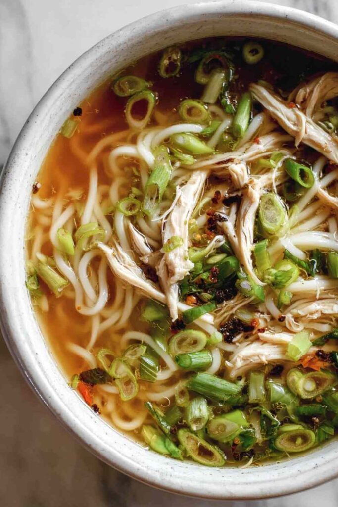 Bowl of ginger garlic chicken noodle soup topped with green onions and fresh cilantro