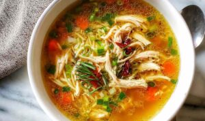 Healing ginger garlic chicken noodle soup in a white bowl garnished with green onions and sesame seeds