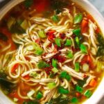 Healing ginger garlic chicken noodle soup in a white bowl garnished with green onions and sesame seeds
