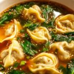 Bowl of homemade wonton soup with beef and shrimp wontons in clear broth garnished with green onions and cilantro