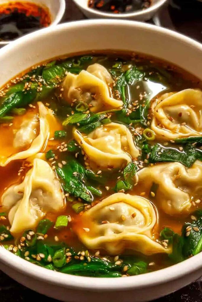 Bowl of homemade wonton soup with beef and shrimp wontons in clear broth garnished with green onions and cilantro