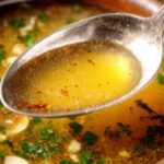 Close-up bowl of Mexican Garlic Soup topped with cotija cheese, diced avocado, fresh cilantro, and crispy tortilla strips