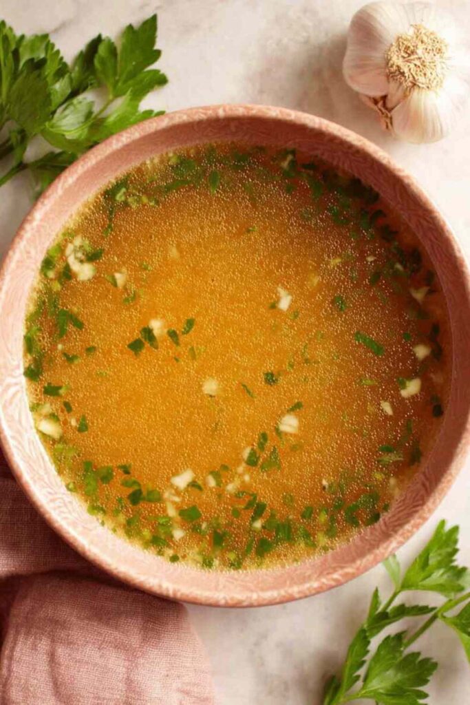 A bowl of Mexican garlic soup topped with fresh cilantro, lime wedges, and crumbled queso fresco