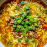 One-pot egg roll soup with ground pork, green onions, and sesame seeds in a white bowl