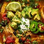 Bowl of poblano chicken tortilla soup topped with diced avocado, sour cream, shredded cheese, and crispy tortilla strips