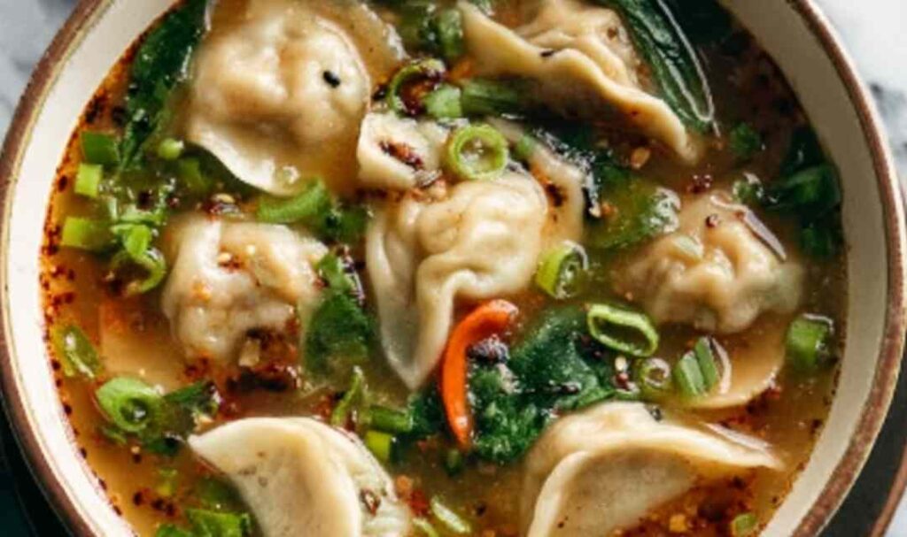 Potsticker soup in a white bowl with spinach, green onions, and chili crisp on top