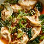 Potsticker soup in a white bowl with spinach, green onions, and chili crisp on top
