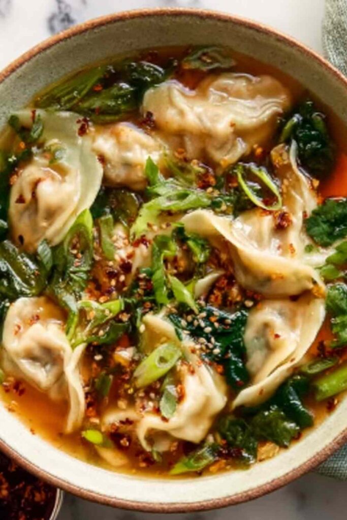 Potsticker soup in a white bowl with spinach, green onions, and chili crisp on top