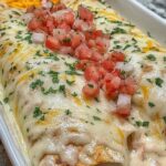 Queso chicken enchiladas in a baking dish topped with melted cheese and fresh cilantro