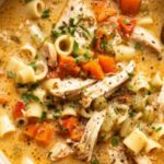 A bowl of Sicilian chicken soup with tender chicken, spinach, carrots, and tomato broth topped with fresh basil and Parmesan cheese