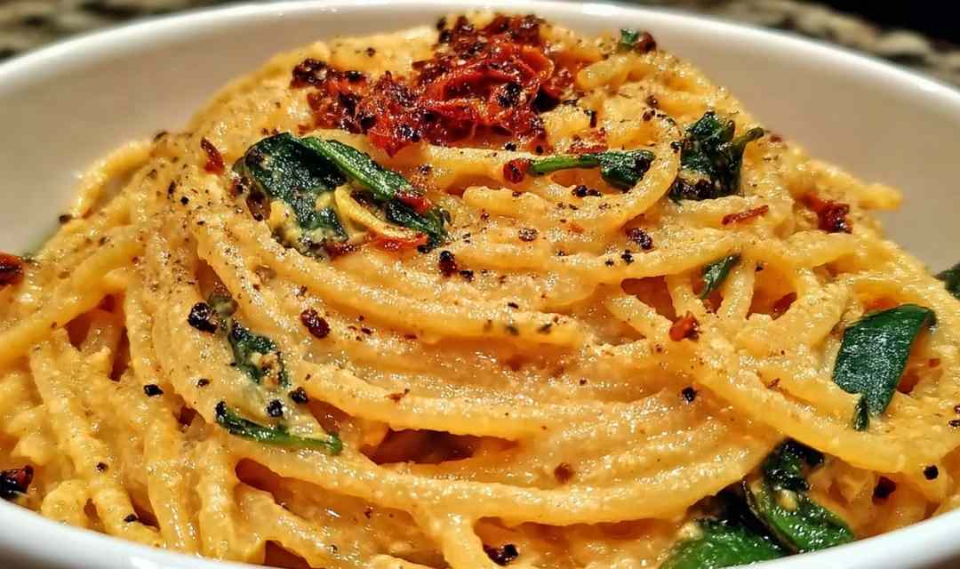 Spaghetti spinach with sun-dried tomato cream sauce served in a white bowl topped with fresh basil and Parmesan