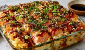 Spicy salmon sushi bake in a white casserole dish topped with avocado, cucumber, green onions, and sesame seeds