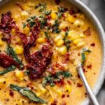 A bowl of creamy Sun-Dried Tomato Corn Chowder topped with fresh basil and a drizzle of cream