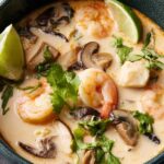 A bowl of Thai coconut soup with chicken, mushrooms, and red bell pepper garnished with fresh cilantro and a lime wedge