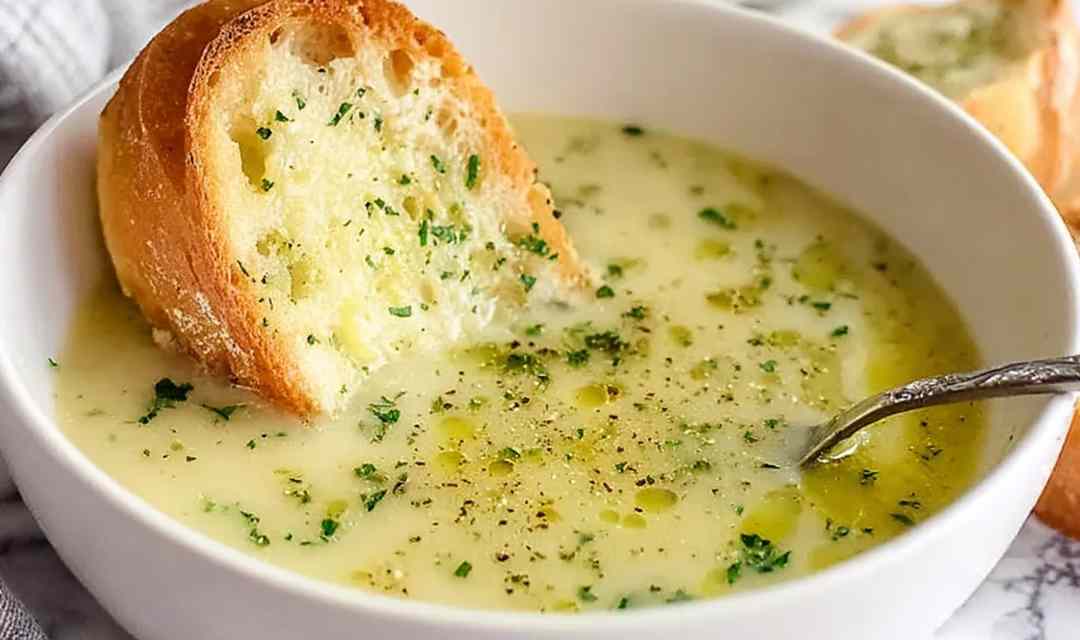 A bowl of traditional country French-style garlic soup garnished with fresh parsley and a slice of toasted baguette