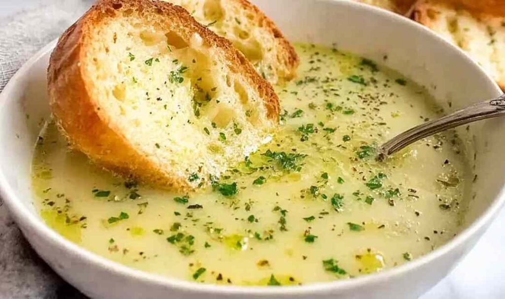 A bowl of traditional country French-style garlic soup garnished with fresh parsley and a slice of toasted baguette