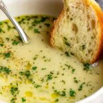 A bowl of traditional country French-style garlic soup garnished with fresh parsley and a slice of toasted baguette