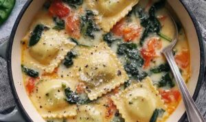 Tuscan ravioli soup in a white bowl topped with Parmesan cheese and wilted kale