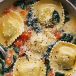 Tuscan ravioli soup in a white bowl topped with Parmesan cheese and wilted kale