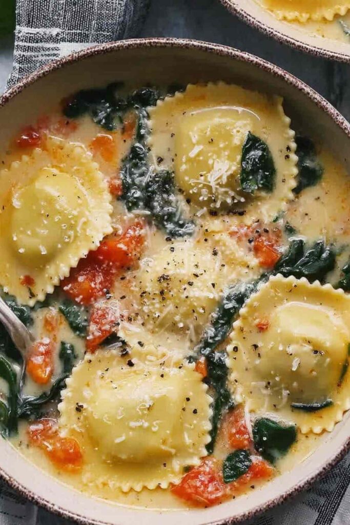 Tuscan ravioli soup in a white bowl topped with Parmesan cheese and wilted kale