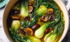 Warming bok choy soup with garlic and ginger in a white bowl garnished with green onions and sesame seeds
