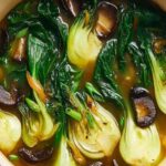 Warming bok choy soup with garlic and ginger in a white bowl garnished with green onions and sesame seeds