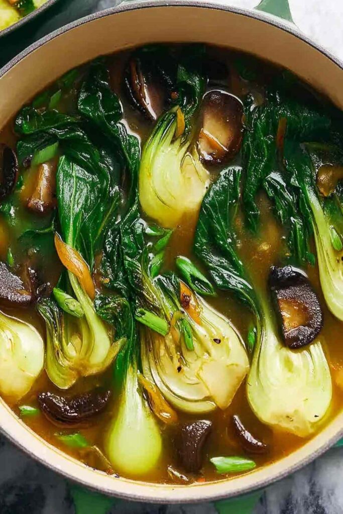 Warming bok choy soup with garlic and ginger in a white bowl garnished with green onions and sesame seeds
