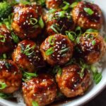 Baked Asian chicken meatballs coated in sticky honey sesame glaze garnished with toasted sesame seeds and green onions in a white bowl over rice
