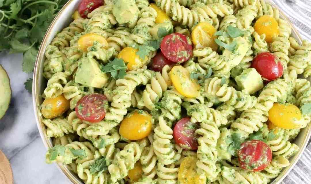 Creamy avocado pasta salad in a large white bowl topped with cherry tomatoes and fresh cilantro