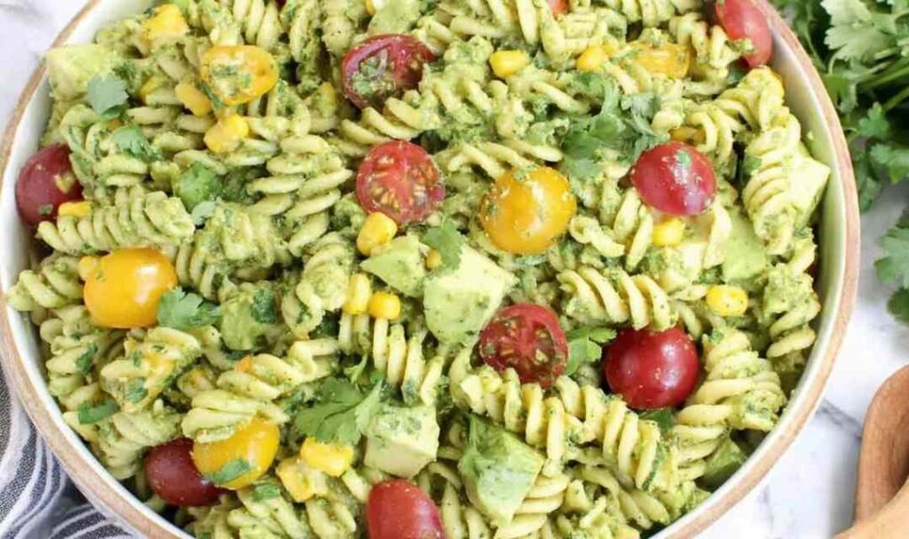 Creamy avocado pasta salad in a large white bowl topped with cherry tomatoes and fresh cilantro