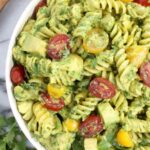 Creamy avocado pasta salad in a large white bowl topped with cherry tomatoes and fresh cilantro