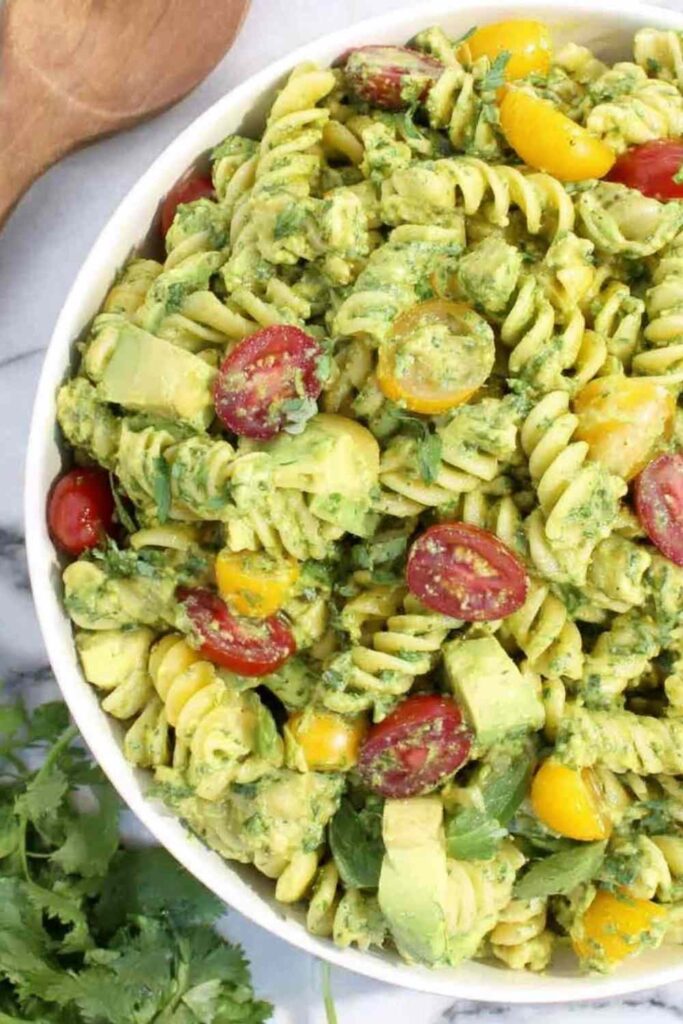 Creamy avocado pasta salad in a large white bowl topped with cherry tomatoes and fresh cilantro