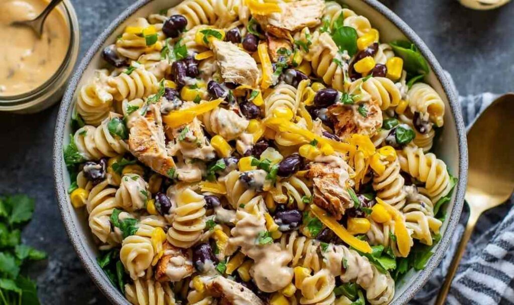 BBQ chicken pasta salad in a large white bowl with corn, red bell pepper, and fresh cilantro garnish