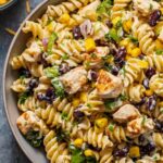 BBQ chicken pasta salad in a large white bowl with corn, red bell pepper, and fresh cilantro garnish