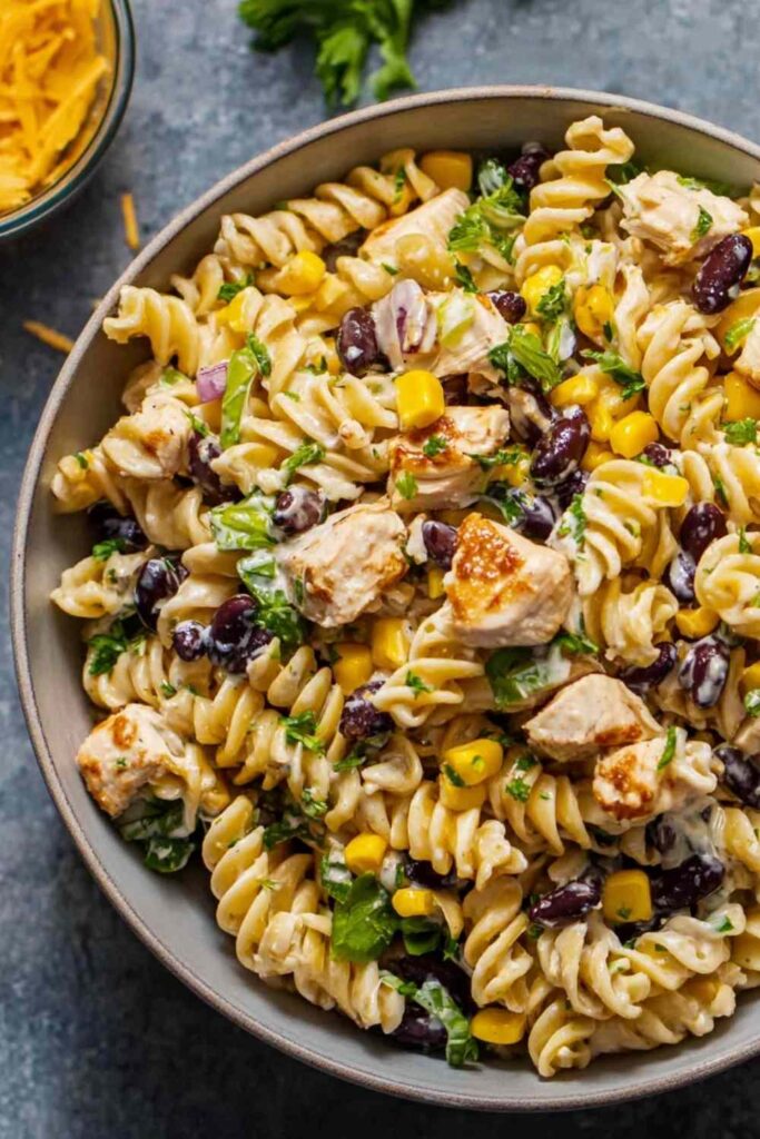 BBQ chicken pasta salad in a large white bowl with corn, red bell pepper, and fresh cilantro garnish